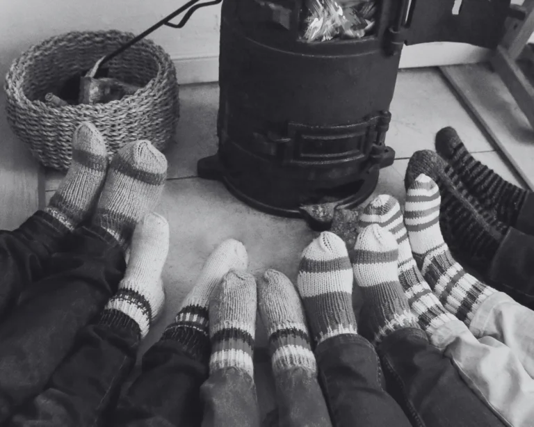 Photo noir et blanc de pieds d'enfants avec des chaussettes en laine devant un poêle à bois